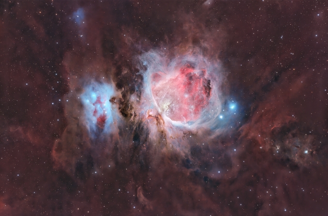 Nel grande respiro della regione di Orione, M42 non è sola: è un cuore luminoso immerso in un paesaggio più vasto, dove vapori cremisi e veli azzurri si dissolvono lentamente nellombra. - Copyright: Massimo Botti & Giuseppe Capriotti 