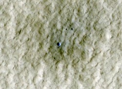 Al centro di questo quadro che raffigura una zona a media-latitudine nell'emisfero nord di Marte, un nuovo cratere di circa 6 metri di diametro (20 piedi) racchiude una esposizione di materiale più luminoso, rappresentato in blu in questa immagine a falsi colori. Credit: NASA/JPL-Caltech/University of Arizona